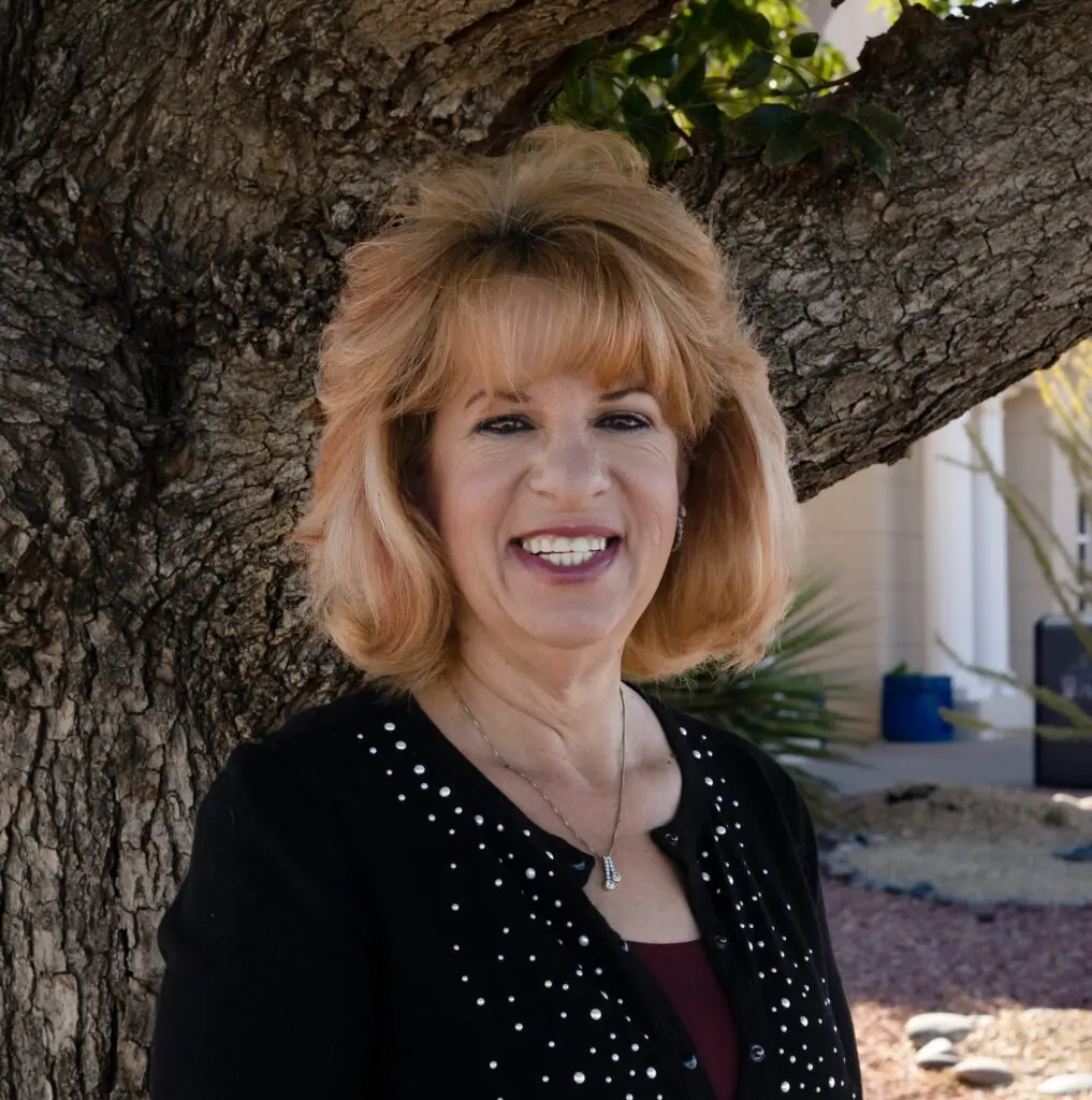 A woman standing next to a tree smiling for the camera.